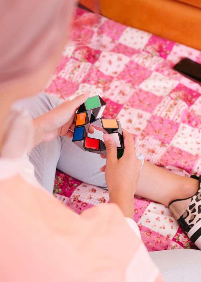 From above back view of female in trendy wear sitting on cozy bed and entertaining with colorful plastic toy while relaxing during weekend at home